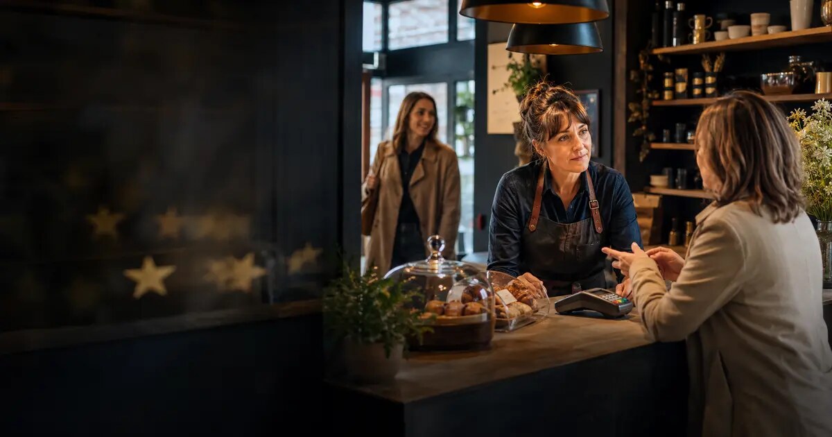 Independent UK business owner listening carefully to a customer at a café counter
